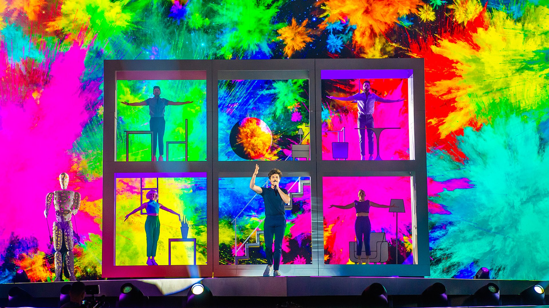 Imagen de Miki Núñez frente a una estantería gigante blanca y un fondo de colores cantando "La venda" en el Festival de Eurovisión 2019