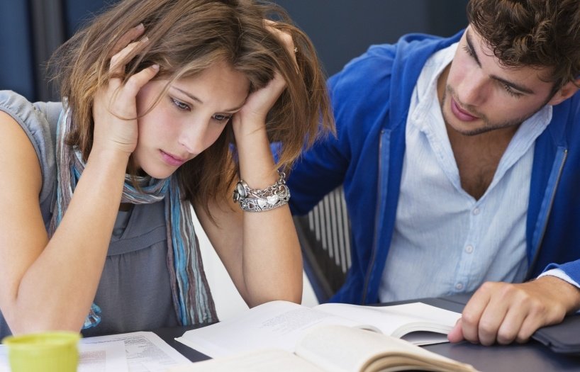 Shows one stressed student looking on her study books and a friend try to support her.